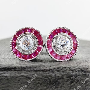 Può includere: Un paio di orecchini a lobo in argento con una pietra centrale rotonda e trasparente circondata da un alone di pietre rosse più piccole.