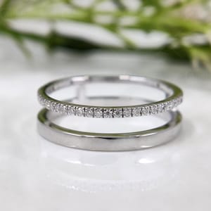 May include: A silver-toned double band ring featuring one thin band encrusted with a row of small, clear, round-cut stones and a second, slightly thicker, smooth, polished solid band connected by a small vertical bridge.