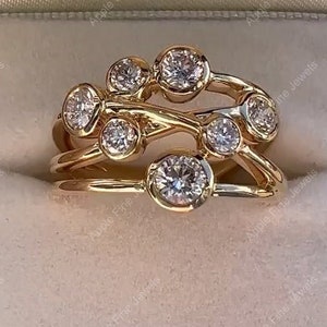 Può includere: Un anello in oro dal design a fasce multiple con sei pietre chiare rotonde incastonate a lunetta disposte a grappolo. Le fasce in oro lucido si sovrappongono e si intrecciano, creando una struttura aperta e stratificata.