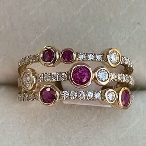 Puede incluir: Un anillo de oro con tres bandas de pequeños diamantes y cinco piedras preciosas rojas engastadas en bisel. El anillo es apilable y tiene un diseño moderno.