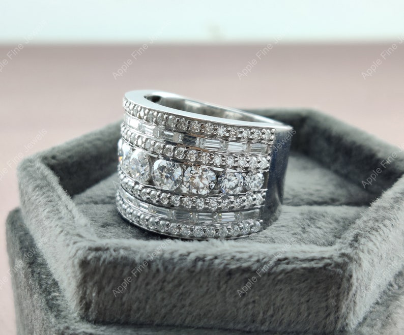 May include: A silver ring with multiple rows of round and baguette-shaped diamonds. The ring is set in a silver band and is displayed on a gray velvet box.