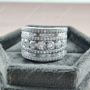 May include: A silver ring with multiple rows of round and baguette-shaped diamonds. The ring is in a gray velvet ring box.