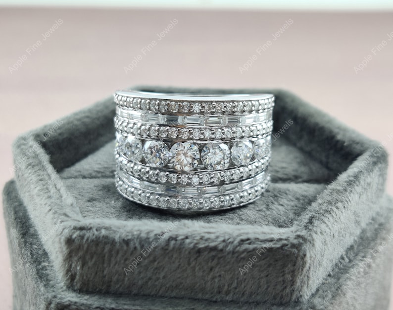 May include: A silver ring with multiple rows of round and baguette-shaped diamonds. The ring is in a gray velvet ring box.