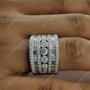 May include: A wide silver band ring with multiple rows of round and baguette-shaped diamonds.