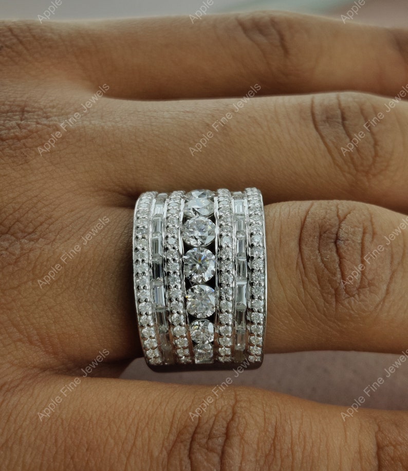 May include: A wide silver band ring with multiple rows of round and baguette-shaped diamonds.