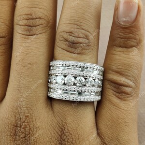 May include: A wide, silver band ring with multiple rows of sparkling diamonds. The ring is set with round and baguette-shaped diamonds.