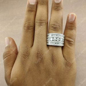 May include: A silver ring with multiple rows of round and baguette-shaped diamonds. The ring is on a person's finger.