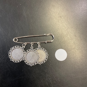 May include: Silver safety pin with three silver round charms with a filigree design. The charms have a blank center that can be used for crafting.