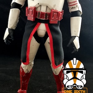 May include: A red and white action figure of a Star Wars clone trooper with a black cape and red boots. The figure has a weathered and battle-damaged appearance. The figure is standing on a black surface. The text "ONE SIXTH CLONES" is visible in the lower right corner of the image.