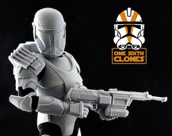 Può includere: Una action figure in plastica bianca di un clone trooper di Star Wars che tiene un fucile blaster. La figura è in piedi su una base nera. La figura indossa un elmetto con una visiera. La figura fa parte della linea di action figure One Sixth Clones.