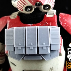 May include: A gray plastic chest rig with five pouches, designed for action figures. The rig is attached to a red and white action figure torso.