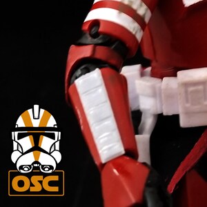 May include: Close-up of a red and white action figure's arm. The figure has white stripes on its red armor. The figure's arm is bent at the elbow.