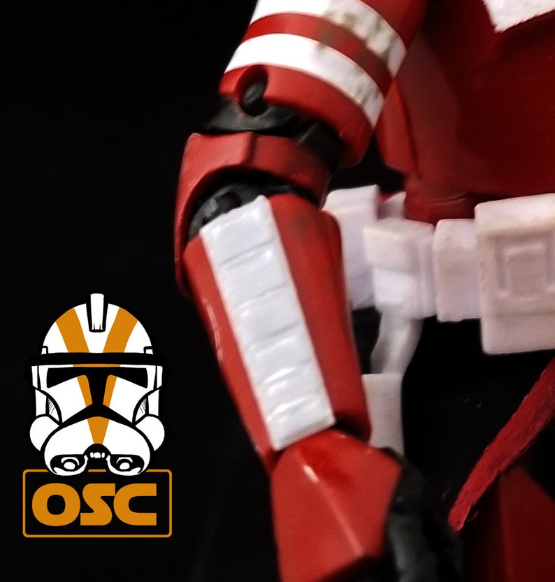 May include: Close-up of a red and white action figure's arm. The figure has white stripes on its red armor. The figure's arm is bent at the elbow.