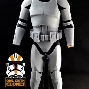 May include: A white plastic action figure of a Star Wars clone trooper. The figure is wearing a white helmet with a black visor and a white armor suit. The figure is standing on a black base.