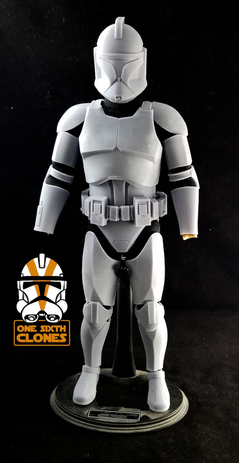 May include: A white plastic action figure of a Star Wars clone trooper. The figure is wearing a white helmet with a black visor and a white armor suit. The figure is standing on a black base.