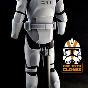 May include: A white plastic action figure of a Star Wars clone trooper, standing on a black stand. The figure is wearing a white helmet and armor, and has a black neck gaiter. The figure is posed with its arms at its sides and its legs slightly apart. The figure is standing on a black stand with a round base. The figure is part of a collection of Star Wars action figures.