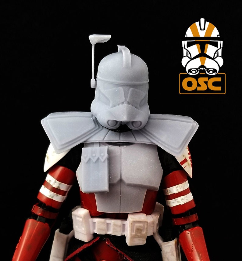 May include: A gray plastic action figure of a Star Wars clone trooper with a red and white chest plate and a gray helmet with a black visor. The figure is wearing a gray shoulder pad and a gray chest piece with a rectangular pouch.