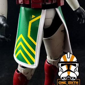 May include: A detailed action figure of a clone trooper, featuring a green and yellow patterned skirt, red accents on the legs, and a maroon belt. The figure has a white and black color scheme with a white border on the skirt. The logo "ONE SIXTH CLONES" is visible.