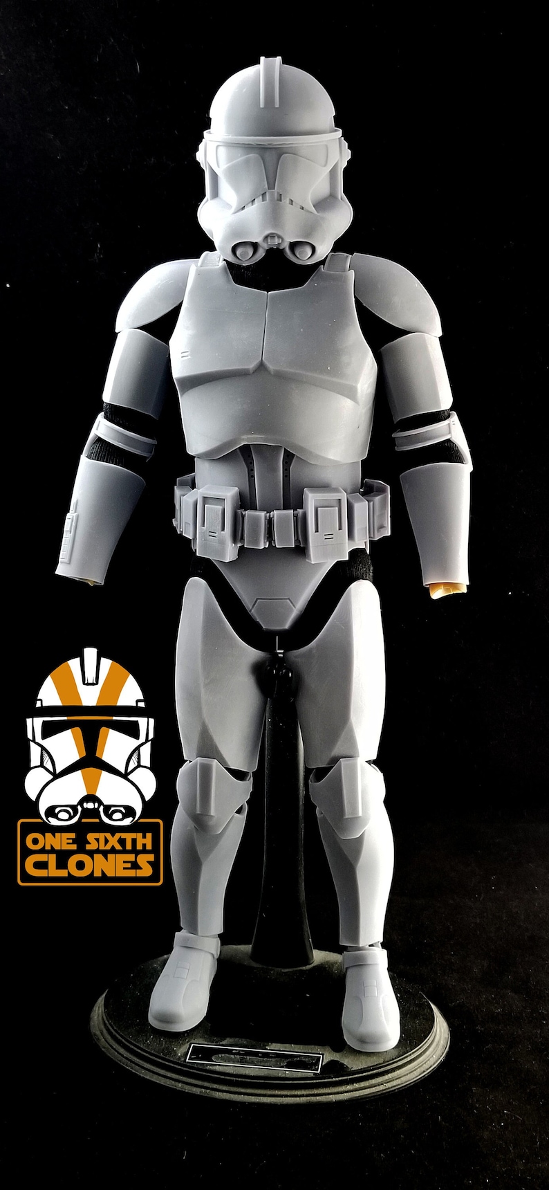 May include: A white plastic action figure of a Star Wars clone trooper. The figure is wearing a helmet and armor, and is holding a blaster rifle. The figure is standing on a black base.