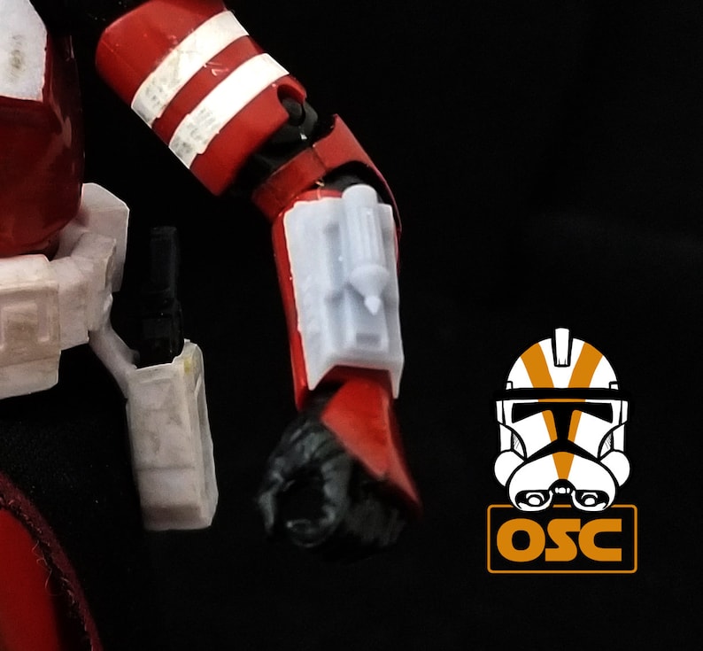 May include: A red and white action figure of a Star Wars clone trooper with a white blaster rifle on its hip and a white and gray accessory on its left arm.