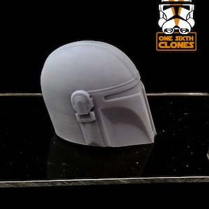 Puede incluir: Un casco de pl&aacute;stico gris con un dise&ntilde;o en relieve en la parte delantera. El casco es una r&eacute;plica de un casco mandaloriano.