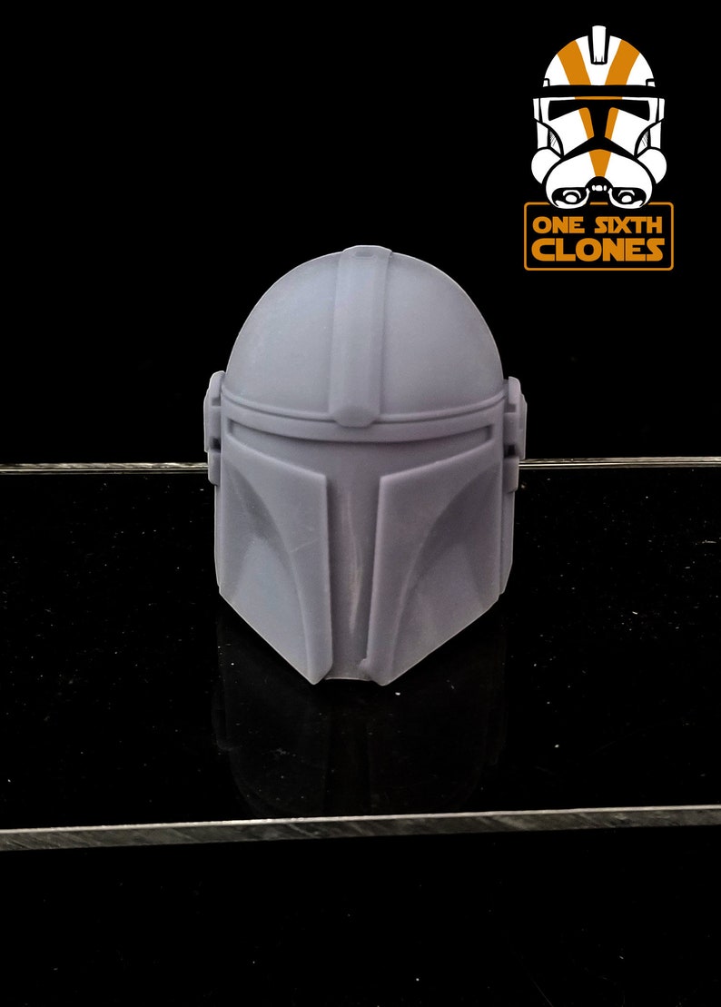 Puede incluir: Un casco mandaloriano de pl&aacute;stico gris para una figura de acci&oacute;n a escala 1/6. El casco tiene una superficie texturizada y est&aacute; dise&ntilde;ado para parecerse al casco que lleva el personaje de la serie Star Wars.