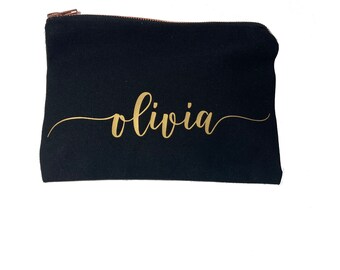 May include: Black canvas zippered pouch with a gold cursive inscription that reads "olivia".