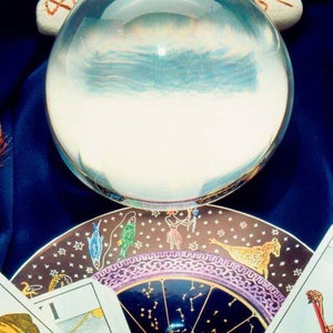 May include: A crystal ball sits on a plate with a zodiac design and tarot cards. The crystal ball is clear and reflects the sky.