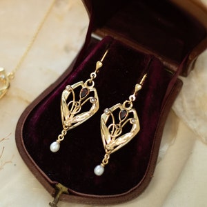 Peut inclure: Un ensemble de collier et boucles d'oreilles en or avec un motif floral délicat et de petites perles. Les bijoux sont présentés dans un écrin en velours bordeaux.