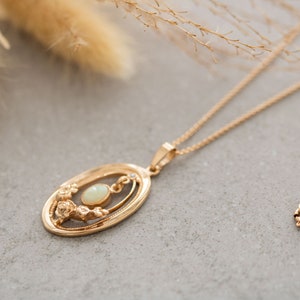 May include: A gold chain necklace with a delicate oval pendant featuring a white opal gemstone surrounded by a floral design.