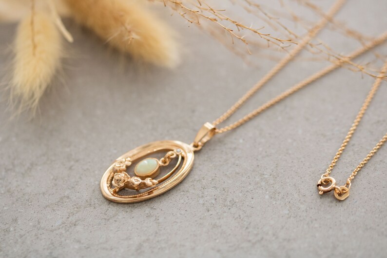 May include: A gold chain necklace with a delicate oval pendant featuring a white opal gemstone surrounded by a floral design.