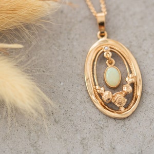 May include: A gold pendant necklace with an oval-shaped frame featuring a delicate floral design and a pale green opal gemstone.