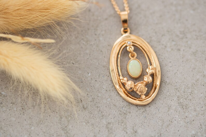 May include: A gold pendant necklace with an oval-shaped frame featuring a delicate floral design and a pale green opal gemstone.