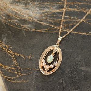 May include: A gold necklace with a delicate oval pendant featuring a light green opal surrounded by smaller sparkling stones.