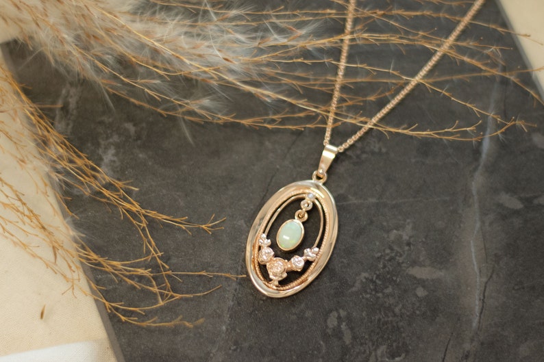May include: A gold necklace with a delicate oval pendant featuring a light green opal surrounded by smaller sparkling stones.