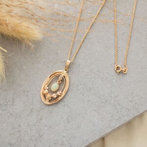 May include: A gold chain necklace with a pendant featuring a delicate oval-shaped opal stone surrounded by a floral design.