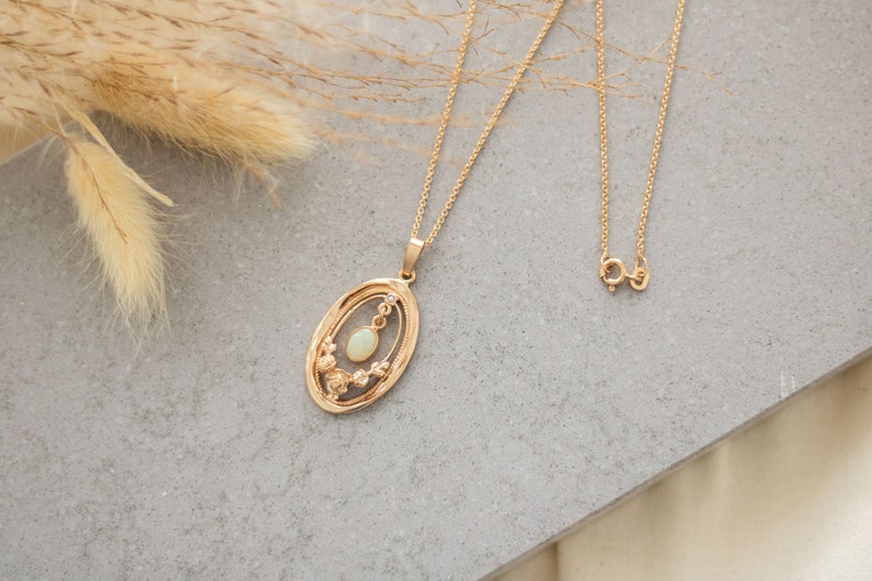 May include: A gold chain necklace with a pendant featuring a delicate oval-shaped opal stone surrounded by a floral design.
