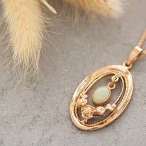 May include: A gold necklace with an oval pendant featuring a delicate floral design and a white opal gemstone.