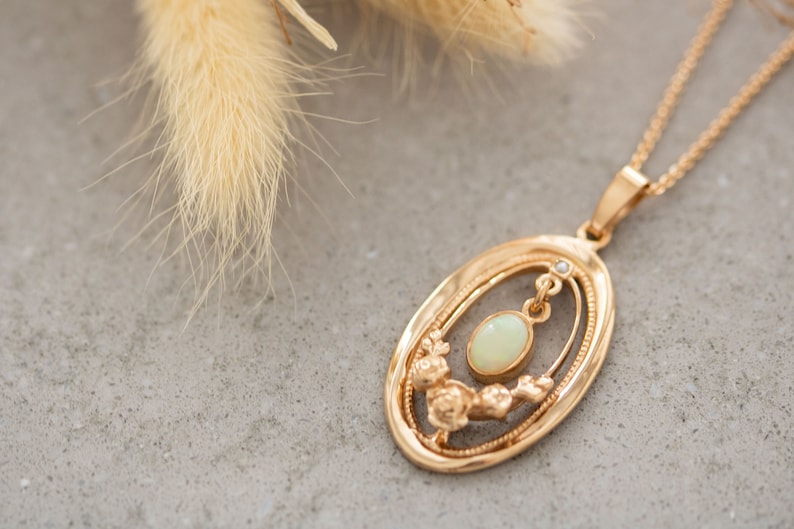 May include: A gold necklace with an oval pendant featuring a delicate floral design and a white opal gemstone.