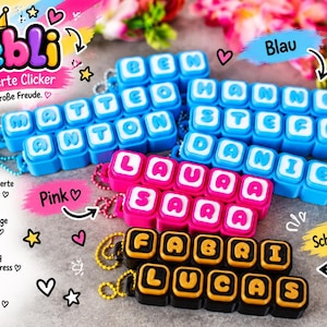 Può includere: Una collezione di portachiavi clicker rettangolari in plastica con nomi personalizzati in lettere bianche. I portachiavi sono disponibili in blu, rosa e nero con accenti dorati, ognuno fissato a una piccola catenella a palline in metallo.