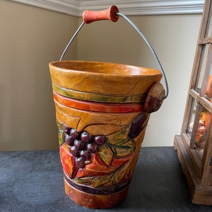 May include: A wooden bucket with a metal handle, painted with a grapevine design in shades of red, orange, green, and purple.