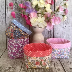 May include: Three fabric storage baskets with floral patterns and contrasting polka dot linings. One basket features a dark floral print with a light blue polka dot rim, another has a purple floral print, and the third has a light floral print with a coral polka dot rim.