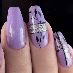 Op de afbeelding: Close-up van gemanicuurde nagels in een lichtpaarse tint. E&eacute;n nagel heeft een zilveren glitterband met zwarte bladeren. Een andere nagel is effen lichtpaars. De nagels hebben een glanzende afwerking.