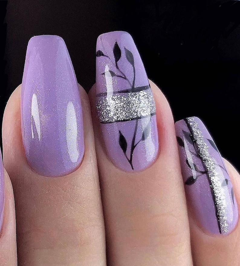 Op de afbeelding: Close-up van gemanicuurde nagels in een lichtpaarse tint. E&eacute;n nagel heeft een zilveren glitterband met zwarte bladeren. Een andere nagel is effen lichtpaars. De nagels hebben een glanzende afwerking.