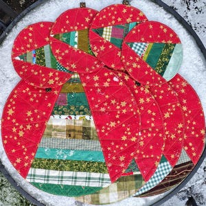 May include: Set of six red and green quilted fabric placemats with a star pattern. The placemats are made of patchwork fabric with different patterns and colors.
