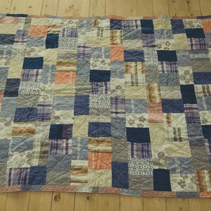 May include: A patchwork quilt with a variety of blue, brown, and orange fabrics. The quilt is made up of squares and rectangles of different sizes and patterns.