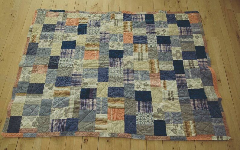 May include: A patchwork quilt with a variety of blue, brown, and orange fabrics. The quilt is made up of squares and rectangles of different sizes and patterns.