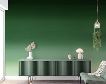 Può includere: Una lunga credenza verde scuro con ante a listelli verticali è posizionata contro una parete con una sfumatura di verde. Sopra vi sono una lampada da tavolo bianca, un piccolo oggetto decorativo e un vaso con foglie di palma essiccate.
