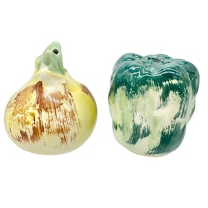 May include: A pair of ceramic salt and pepper shakers shaped like vegetables. One is an onion with yellow, brown, and green hues. The other is a green and white pepper. Both have a glossy finish and are set against a white background.