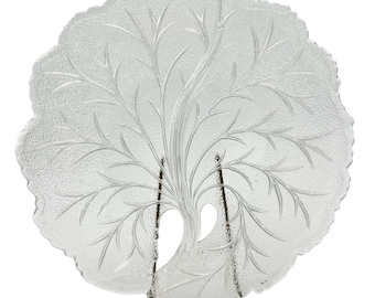 Puede incluir: Un plato decorativo de vidrio transparente con un diseño de hoja. El plato está sostenido por un soporte de metal dorado. El diseño de la hoja presenta vetas grabadas y una superficie texturizada.